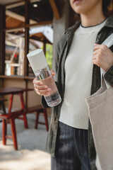 Woman holding reusable water bottle outdoors. Eco friendly lifestyle, zero waste habits, healthy living and hydration concept