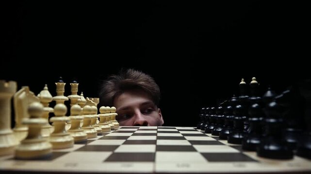 A young man looks out from under the chessboard, thinking about his first move, and then hides under the table.