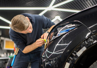 Fototapeta premium A car wrapping specialist applies a polyurethane film to the car. Detailer smoothes PPF. Car wrapping, detailing, tuning and styling. PPF protective film against chips and scratches. Car protection.