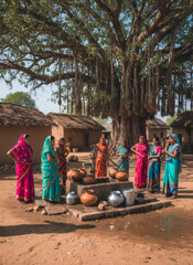 Obraz premium Seven women in colorful saris preparing to collect water from a village pump. Indian rural life and tradition concept for travel marketing.