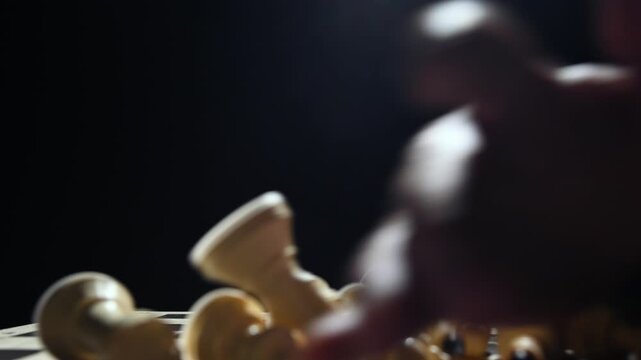 White chess pieces on a black background stand in a row, and the chess player's hand passes over them, knocking them down onto the game board. 4к