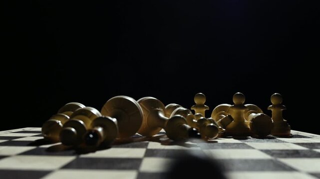 White chess pieces on a black background stand in a row, and the chess player's hand passes over them, knocking them down onto the game board. 4к