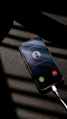 Unknown Incoming call on smartphone charging on a black chair textured surface. Communication and the use of mobile phones concept.