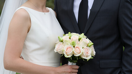 Close-up of Bride Holding Bouquet of Pink Roses and Greenery Next to Groom in Suit during Wedding Ceremony Outdoors