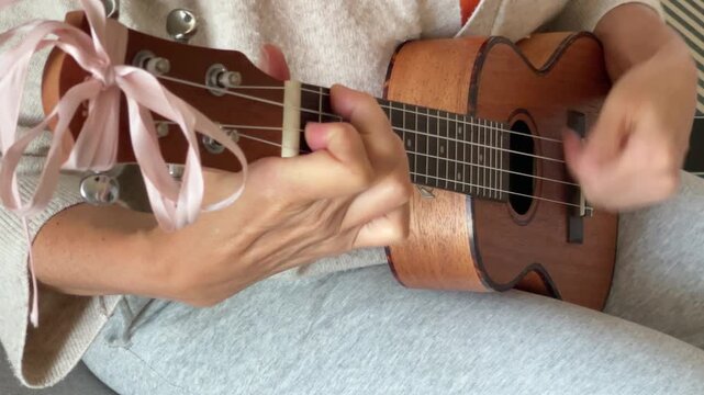 Close up ukulele string instrument popular on Hawaii islands. Woman playing nylon strings during music lessons in living room. Musical education, art, hobby and leisure lifestyle photography concept