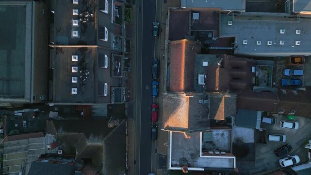 An aerial view captures a street lined with buildings and cars, bathed in the warm glow of sunset.