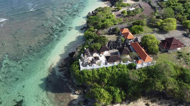 Cinematic aerial drone tilt up revealing cliff temple above Geger Beach in Nusa Dua, Bali, Indonesia.