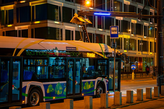 Modern MPK Krakow electric bus featuring "Technology for Ecology" branding against night city architecture. Sustainable public transport in Krakow illuminated by street lights near a contemporary offi