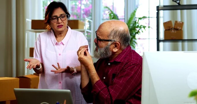 Indian senior couple showing stress doing E-commerce business from home while managing online orders, dispatching parcels, packing cardboard boxes and handling hectic workload in home office