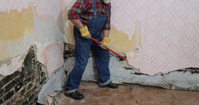 Worker demolishing old building wall using crowbar tool