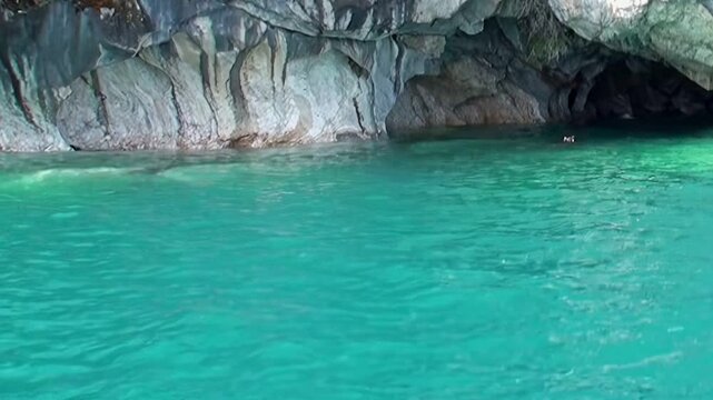 Marvel at Patagonia's wondrous Marble Caves, gleaming with sculpted white and gray patterns. Pristine turquoise waters of General Carrera Lake reflect the majestic natural artistry on a bright day.