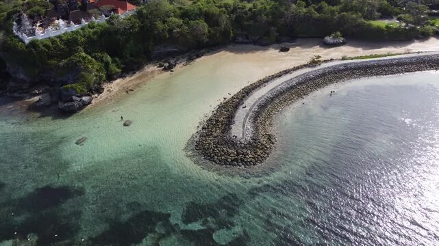 Wide aerial drone orbit right around coastal wave breaker at Geger Beach in Nusa Dua, Bali, Indonesia.