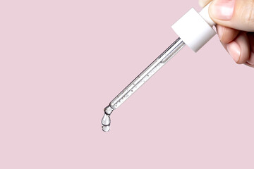 Naklejka premium Pipette with serum in hand. Drips drop isolated on pink background, copy space photo close up