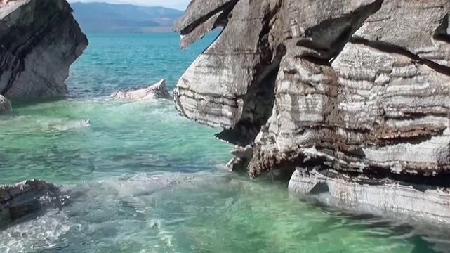 Sunlight illuminates the majestic Marble Caves of Patagonia. Pristine turquoise waters flow around these captivating natural rock formations, showcasing a tranquil, artistic landscape on a bright day.