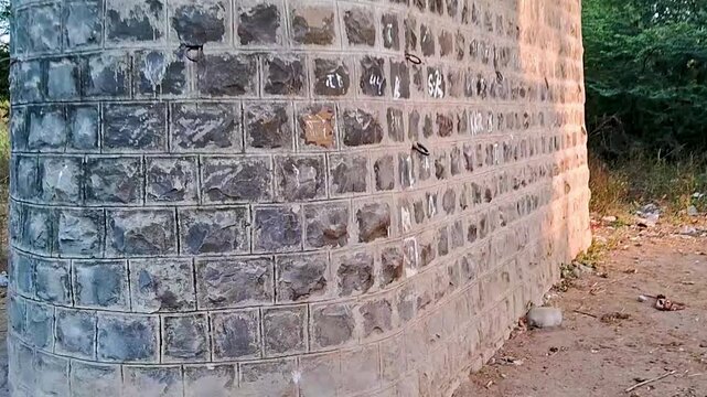 Close-up view of a textured stone brick wall corner in an outdoor rural setting, highlighting masonry details, geometric block patterns, and solid construction structure.