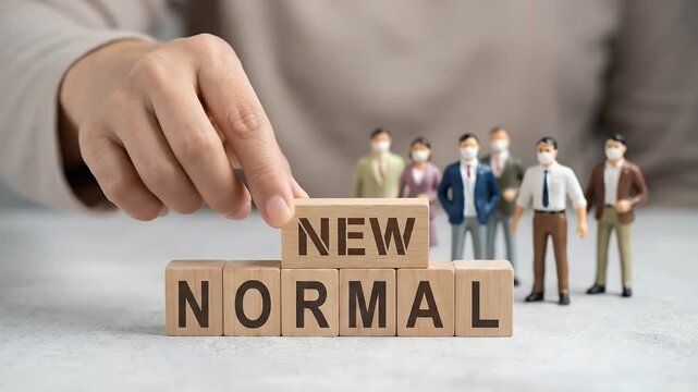 Close-up of a hand positioning a wooden block labeled new above blocks spelling normal, small figurines wearing face masks standing behind, slight downward motion as the block settles, neutral backgro