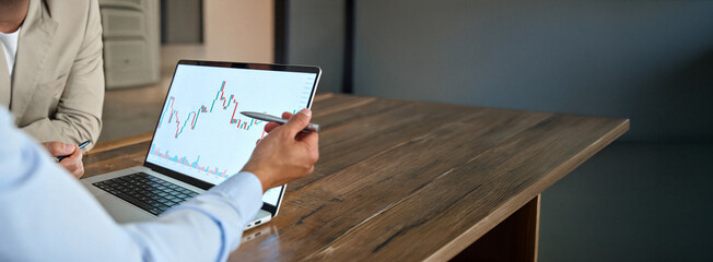 Naklejka premium Financial advisor explaining invest stock market data consulting investor. Two business men analysts doing finance trading analysis pointing at chart on laptop screen working in office. Close up.