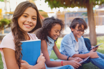Portrait of cute little school girl and children on background with backpacks and notebooks sitting...