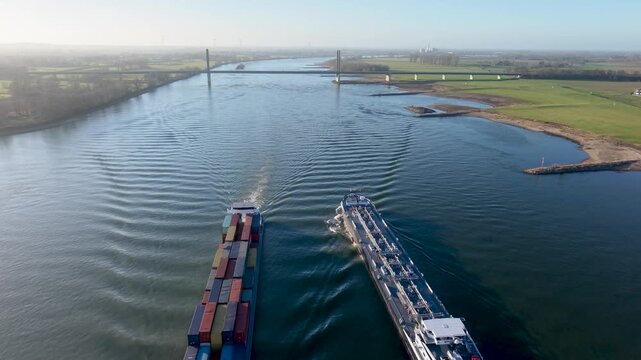 Aerial drone view of a long industrial tanker barge cruising past the historic town of Rees on the Rhine River, Germany. Picturesque riverside architecture and city skyline.
