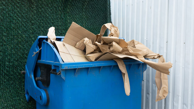 Overfilled blue recycling bin with brown cardboard waste and paper packaging
