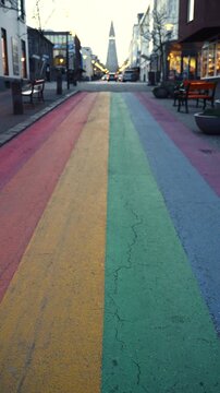 Vertical shot of a rainbow painted street in a Nordic city at sunrise with church in soft bokeh.