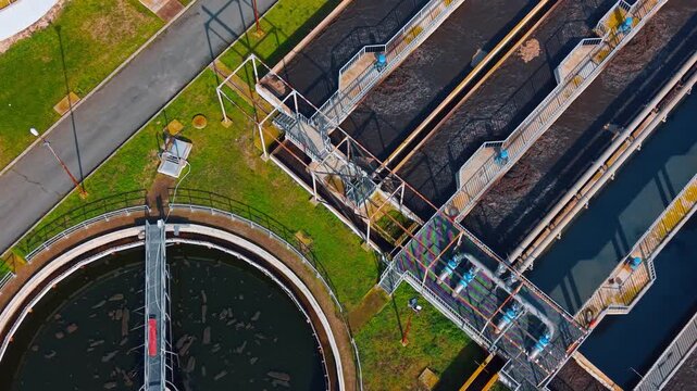 Industrial wastewater treatment plant tanks and aeration systems. Top down view of circular and rectangular clarification tanks with pipes and water filtration systems.