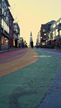 Low angle vertical shot of rainbow street at sunrise with silhouettes of people and church in the background.