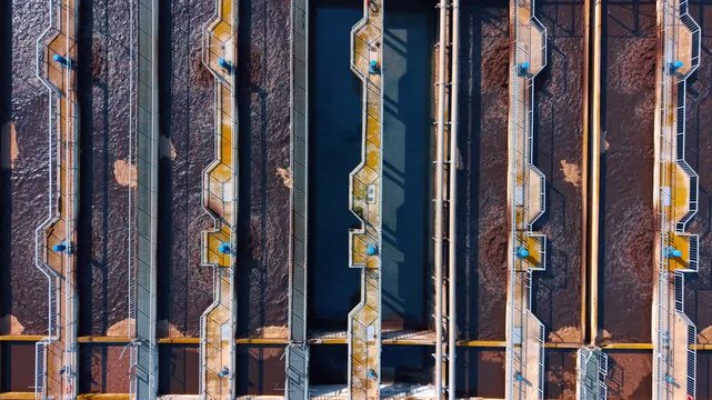Top down view of rectangular aeration tanks in sewage plant. Aerial shot of parallel biological treatment basins with brown activated sludge and walkways.