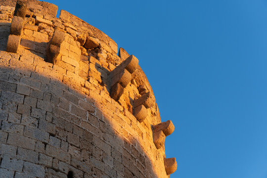 Sunlit stone castle tower with projecting corbels against blue sky