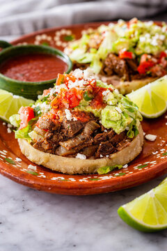 Sope mexicano con carne, guacamole y salsa roja en plato de barro