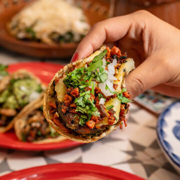 Mano sosteniendo taco de pastor con cilantro y cebolla 