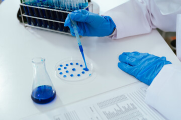Scientist wearing gloves and a lab coat holding test tubes filled with blue liquid in a laboratory, representing scientific research, chemical analysis, and medical experimentation.