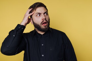 Obraz premium Surprised man on vibrant yellow background expresses shock with open mouth and hand on head, capturing a moment of disbelief