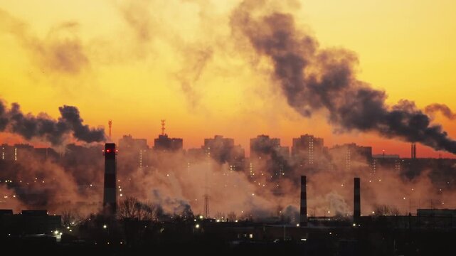 Industrial Chimneys With Steam Clouds Over City Skyline at Sunrise