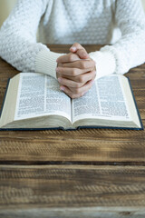 Naklejka premium Praying Hands Over Open Bible. Close-up of hands clasped in prayer over an open Bible. Spiritual devotion, Christian faith, worship, hope, and religious reflection concept with copy space.