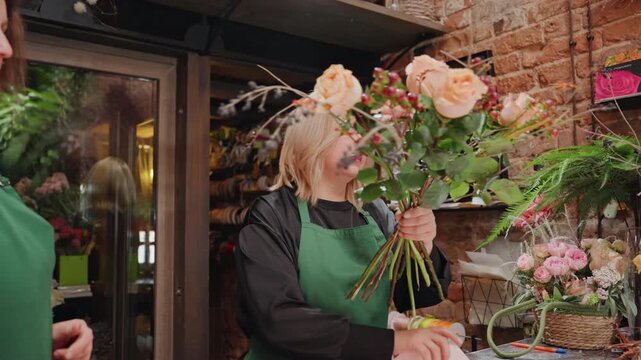 Blonde florist arranging peach rose bouquet in rustic brick workshop, selecting stems trimming leaves wrapping bouquet with craft paper and twine, handson floral design, warm ambient lighting, jars