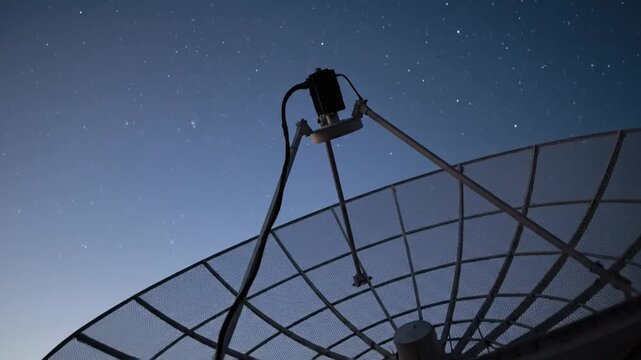 Large satellite dish under a star-filled sky at dusk