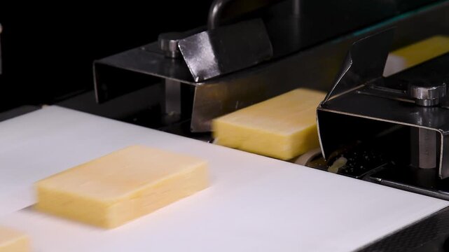Conveyor belt with pieces of yellow cheese moving on it.