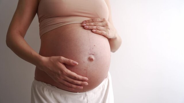 Isolated of impersonal woman body. Young mother touching naked tummy belly at third trimester showing love, care to baby standing at wall. Pregnant, eco, prenatal maternity, motherhood. Copy space