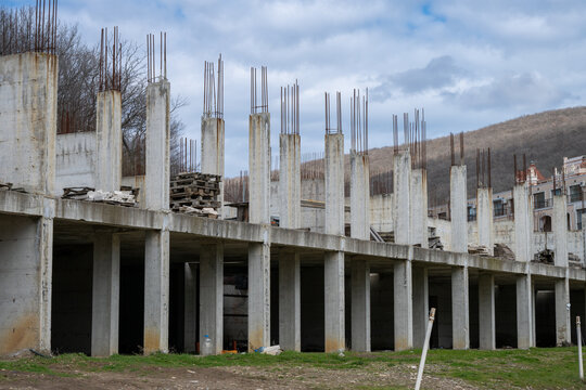 the skeletal remains of a multi-story concrete building under construction or major structural repair, with exposed support pillars and rebar standing against a cloudy sky.