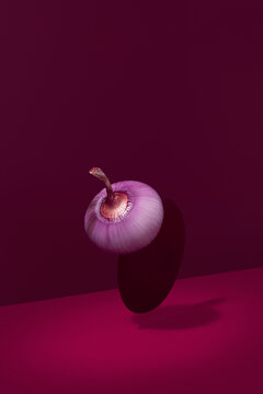 Una Cebolla roja cruda levitando sobre un fondo granate	