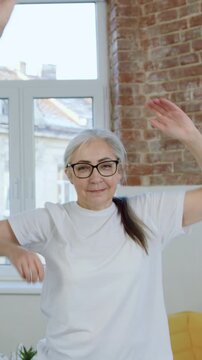 Attractive active positive mature bearded man and his wife in white t-shirts tilting their bodies in both sides in front of camera while doing physical exercises in contemporary apartment