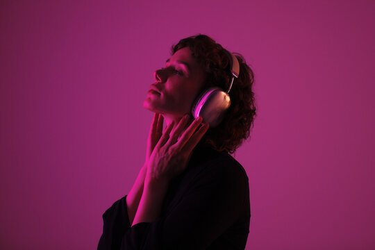 Young woman with headphones in pink neon lighting. Music, emotion, nightlife and modern audio lifestyle concept.