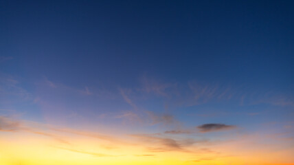 Obraz premium Beautiful golden sunset sky with wispy cirrus clouds at twilight,A breathtaking view of the evening sky during golden hour, featuring delicate orange and yellow wispy clouds scattered across.