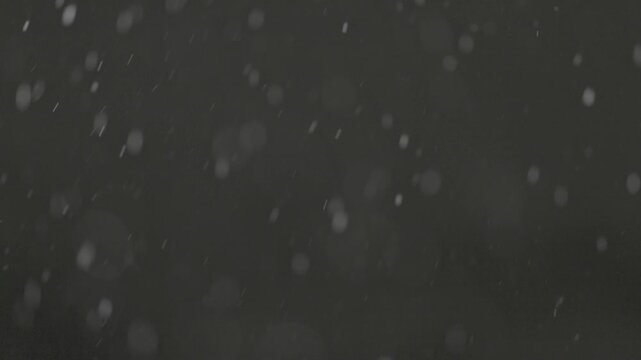 Slow motion falling snow particles on dark background, cinematic winter atmosphere with dense blizzard effect, swirling flakes, bokeh for overlays. ProRes 422, 10 bit ungraded C-LOG2, Slow motion vide