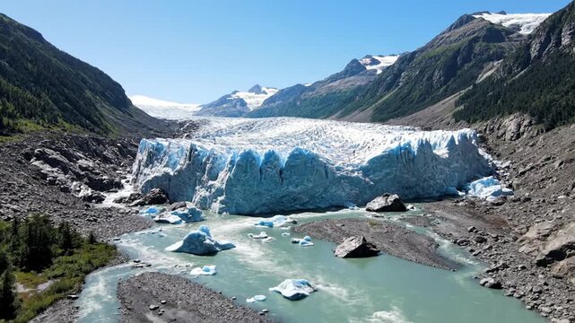 Massive blue glacier with glacial river and icebergs in mountain valley