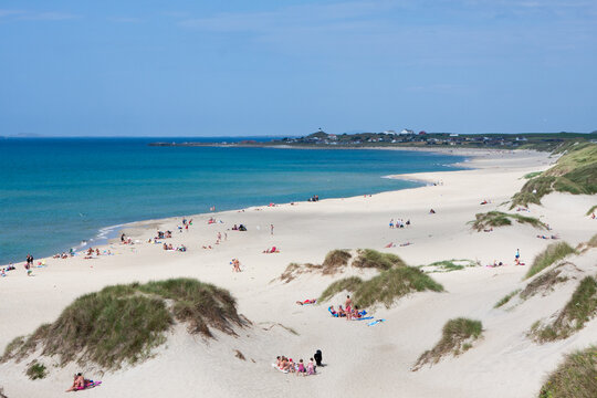 Many visitors spend a sunny day at Borestranda beach in Kleppe, Norway. People relax on the sand, swim, and play along the water's edge. The beach is busy with activities.