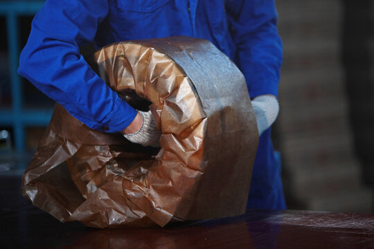 Worker packs the finished bearing. Oiled parchment for packaging metal products. Finished products at the factory. Heavy industry. A workshop at a heavy industry plant.