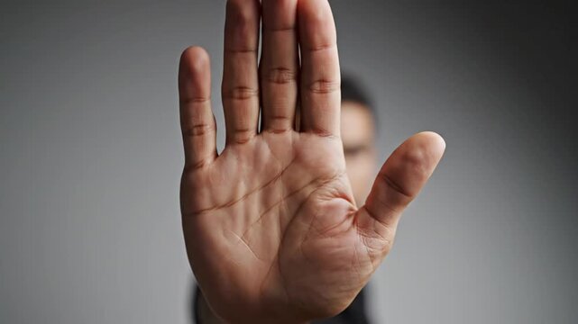 Person showing open palm in stop gesture against gray background