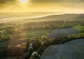 Zachwycająca panorama pagórkowatych pól i lasów w złotej godzinie. Widok z lotu ptaka na wiosenny krajobraz skąpany w ciepłym, mglistym świetle zachodzącego słońca. © Henryk Niestrój